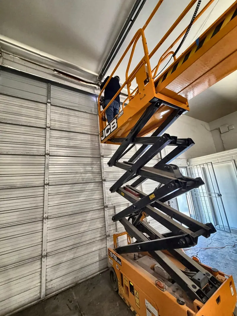 Technician on a scissor lift repairing a tall commercial roll-up door
